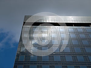 Modern contemporary high-rise office building exterior against blue sky with clouds. Reflection of sky on glass windows of