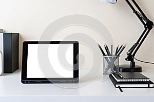 Modern contemporary workspace with mockup blank screen tablet computer and office supplies on white table. Front view of workplace