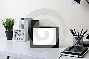 Modern contemporary workspace with mockup blank screen tablet computer and office supplies on white table. Front view of workplace