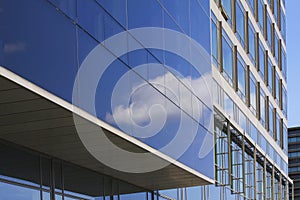 Modern corporate highrise building with glass facade reflecting sky with clouds