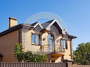 Modern cottage with forgery balcony and brick facade. Blue sky background