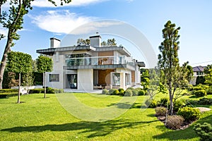 Modern country house with the large lawn and a wooden fence. In front of the house there is a covered terrace with a lounge zone.