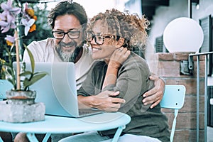 Modern couple enjoying video call on laptop sitting outside home in the garden. Wireless connection. People man and woman using