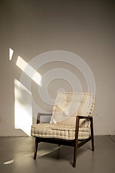 Modern cozy armchair stands in empty room against beige wall. Interior items. Minimalism simplicity.