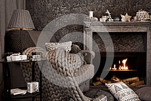 Modern cozy interior in gray shades with an armchair in front of fireplace.