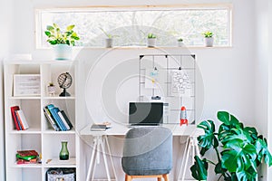 Modern cozy light workplace - white desk with laptop black screen, grid mood board with pinned notes, shelves with docs