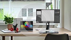 Modern creative office studio interior with laptop, blank screen computer, graphic tablet and stationery on wooden table