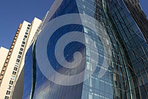 Modern curved blue corporate building next to a yellowish classical one.