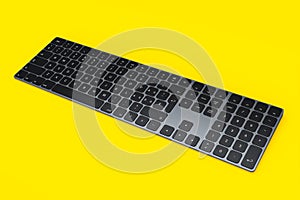 Modern dark aluminum computer keyboard isolated on yellow background.