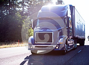 Modern dark big rig blue semi truck with trailer on the road in