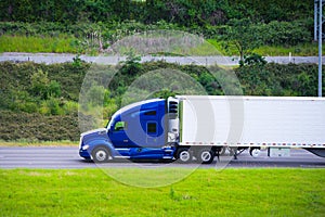 Modern dark blue semi truck reefer trailer profile on green road