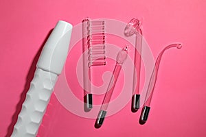 Modern darsonval with different nozzles on pink background, flat lay. Microcurrent therapy