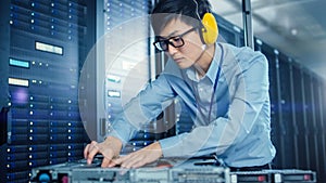 In the Modern Data Center: IT Engineer Wearing Protective Headphones Installs New Hardware for Ser