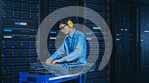 In the Modern Data Center: IT Technician Wearing Protective Headphones Working with Server Racks,