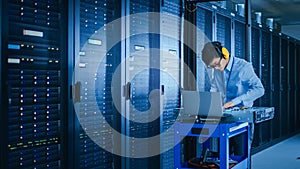 In the Modern Data Center: IT Technician Wearing Protective Headphones Working with Server Racks,