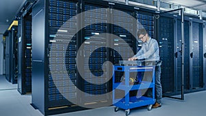 In the Modern Data Center: IT Technician Working with Server Racks, on a Pushcart Various Equipmen