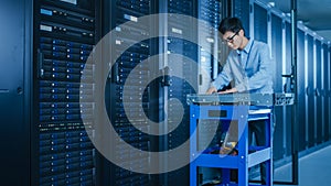 In the Modern Data Center: IT Technician Working with Server Racks, on a Pushcart Various Equipmen