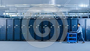 In the Modern Data Center: IT Technician Working with Server Racks, Pushes Cart Between Rows of Se