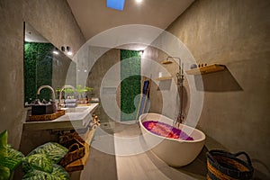 Modern design of bathroom with free standing oval bathtub, bidet, wooden cabinet with utensils and panoramic window
