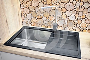 Modern design chrome water tap over stainless steel kitchen sink on table top made of natural wood with surface behind countertop