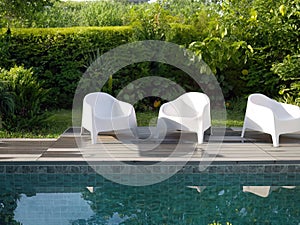 Modern design white plastic chairs at swimming pool side and outdoor garden, comfortable veranda decorated, wooden deck, back yard