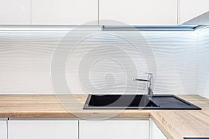 Modern designer chrome water tap over black new kitchen sink. The working area of the kitchen surface is made of wood. Table top m