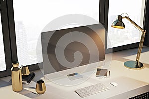 Modern designer desktop with empty computer monitor, lamp, supplies and other items. Window with city view in the background. Mock