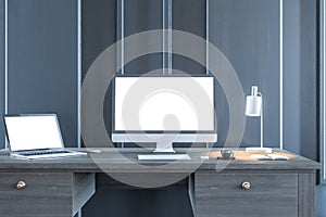 Modern designer desktop with empty white computer and laptop screens in wooden interior at night. Workplace concept. Mock up, 3D