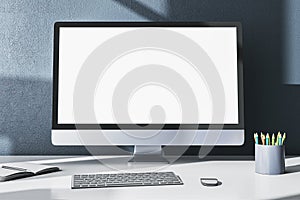 Modern designer office desktop with empty white mock up computer monitor, supplies and other items on gray wall background. 3D