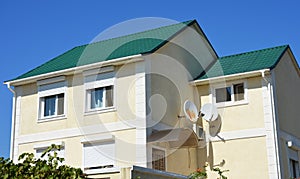 A modern detached house with a green metal roof, stucco, plastered painted walls, windows with closed plastic rolling shutters,