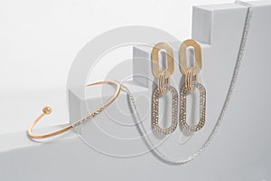 Modern diamond bracelet and earrings pair on white geometric stairs background