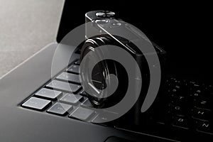 Modern digital camera on laptop keyboard on black desk in office, digital photography or image processing concept