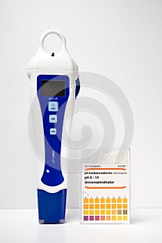 A modern digital pH meter next to a box of paper pH strips. pH measuring.