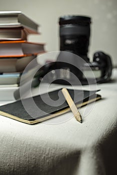 Modern digital SLR camera on the table next to a stack of books, and in the foreground a notebook and pencil.