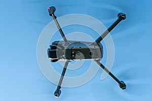 A modern drone against a clear blue sky. The quadcopter hovered motionless in the sky. The use of aircraft for reconnaissance and