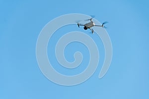 A modern drone against a clear blue sky. The quadcopter hovered motionless in the sky. The use of aircraft for reconnaissance and