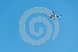 A modern drone against a clear blue sky. The quadcopter hovered motionless in the sky. The use of aircraft for reconnaissance and