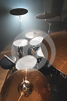 Modern drum set prepared for playing in a dark rehearsal room on stage with a bright spotlight. The concept of