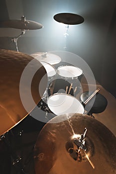 Modern drum set prepared for playing in a dark rehearsal room on stage with a bright spotlight. The concept of