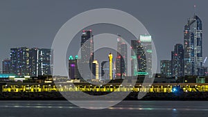 Modern Dubai city skyline timelapse at night with illuminated skyscrapers over water surface