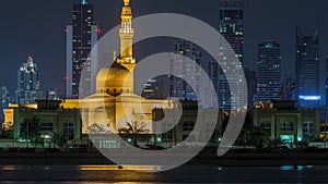 Modern Dubai city skyline timelapse with Rashid Al Hadeeth Mosque at night with illuminated skyscrapers over water photo