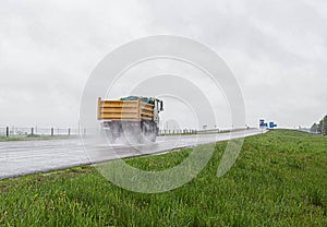 A modern dump truck for transporting bulk cargo drives on the highway in rainy weather. Safe driving in bad weather