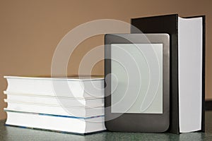 Modern e-book on the background of a stack of thick paper books. Close-up with selective focus
