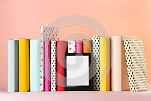 Modern e-book reader and hard cover books on pink