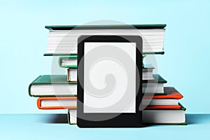 Modern e-book reader and stack of hard cover books on light blue background