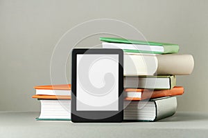 Modern e-book reader and stack of hard cover books on light grey table