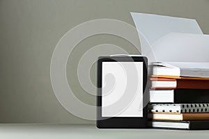 Modern e-book reader and stack of hard cover books on light grey table. Space for text
