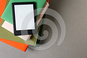 Modern e-book reader and stack of hard cover books on light grey table, top view. Space for text