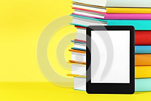 Modern e-book reader and stack of hard cover books on yellow background. Space for text