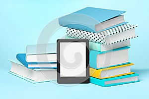Modern e-book reader and stacks of hard cover books on light blue background